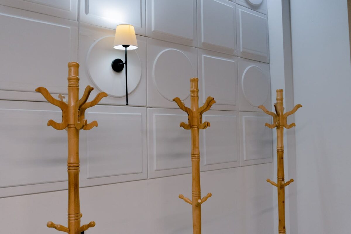 A row of wooden coat racks in front of a stylish paneled wall with a wall lamp.