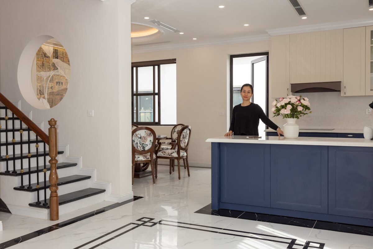 Spacious modern kitchen with a woman standing, elegant floral decor and stylish furniture.